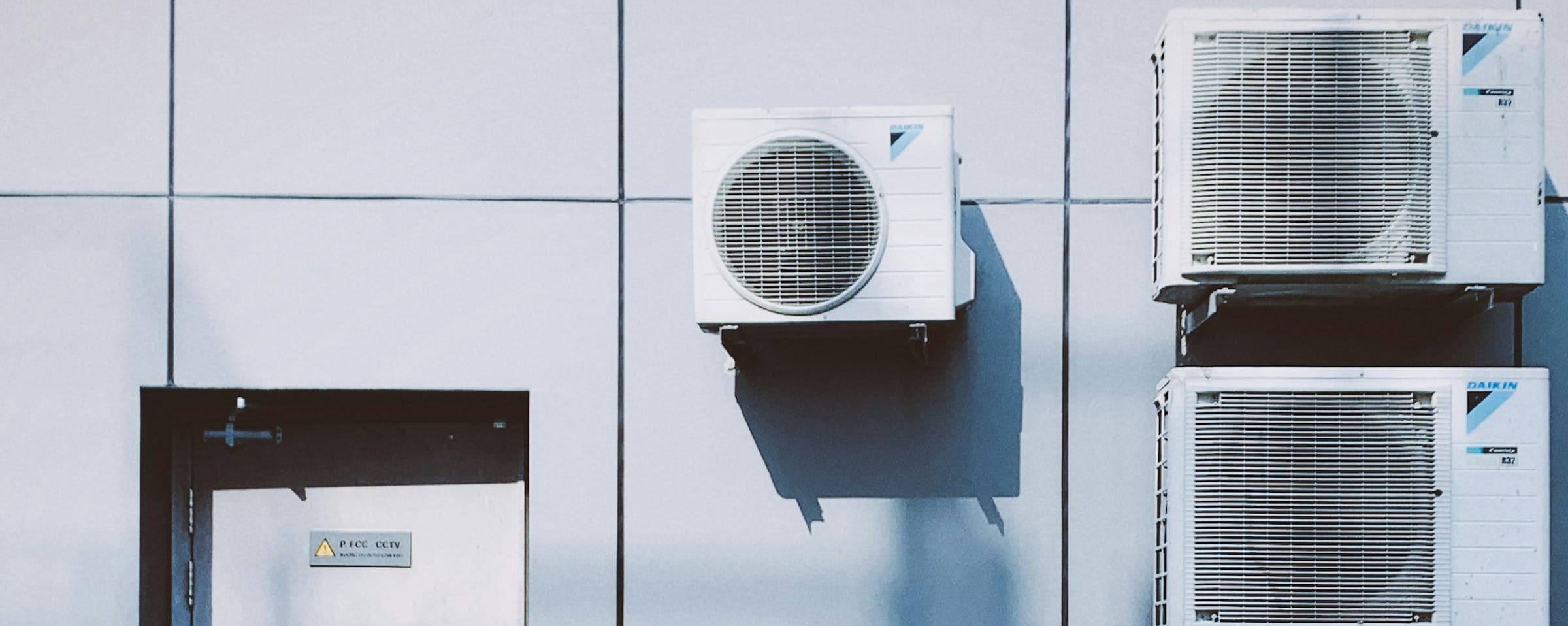 Unité extérieure de climatisation et son ombre portée sur un mur à panneaux.